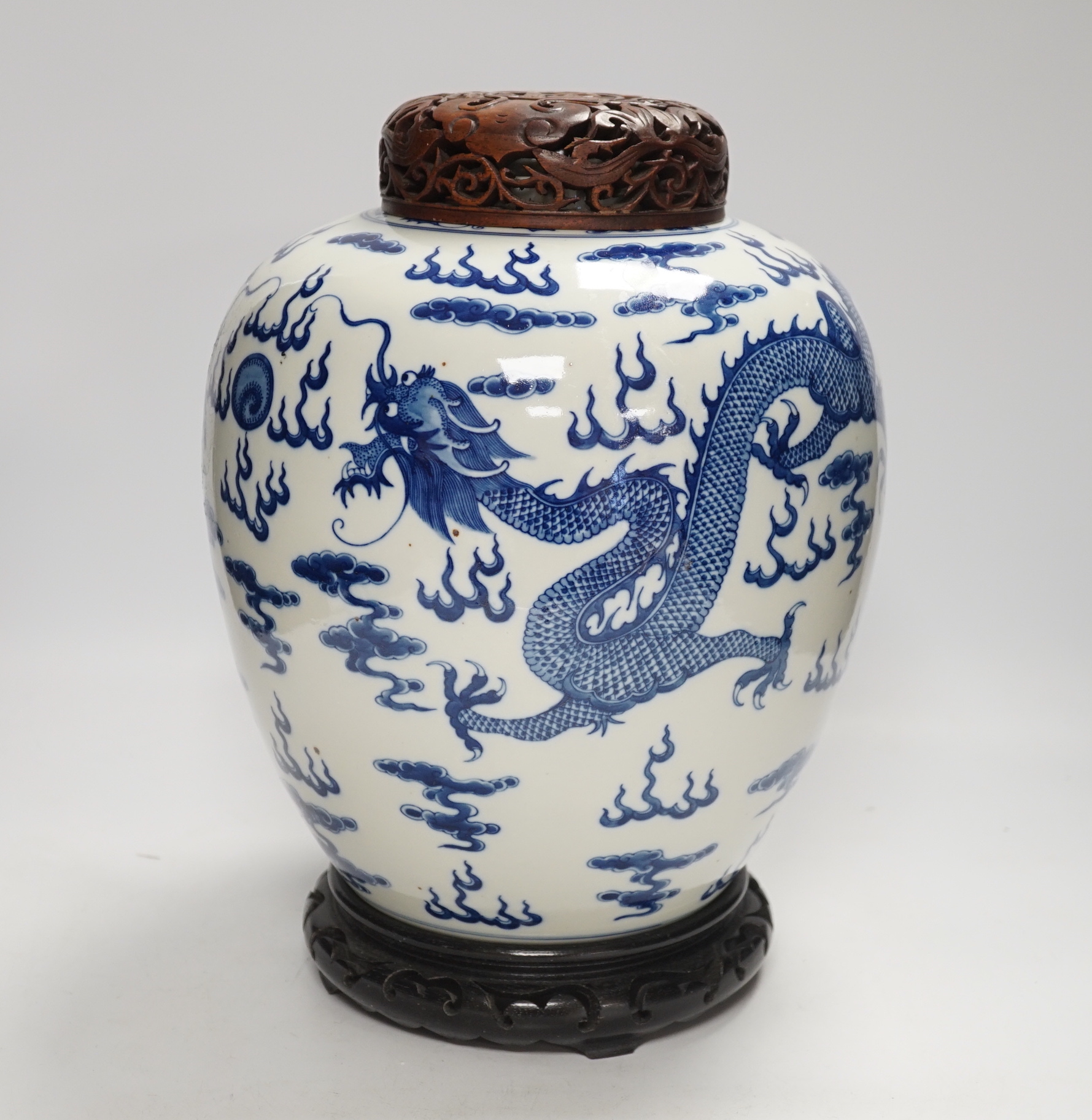 A large Chinese blue and white jar decorated with dragons chasing the flaming pearl together with unassociated carved wood lid and stand, 35cm high